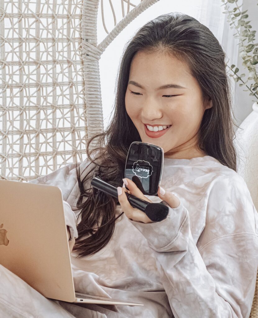 girl on computer holding mascara and compact